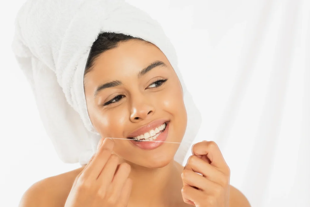 A person with a towel wrapped around their head holds their chin, surrounded by a bright, softly lit background flossing before seeing a dentist on hiatus rd