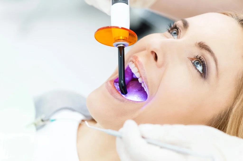 Woman pointing at her perfectly white teeth with both hands, showing confidence after whitening treatment. Teeth whitening in Pembroke Pines